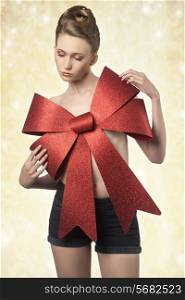 creative christmas portrait of sexy woman adorned like a gift with big red bow on the breast and elegant hair-style