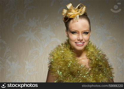 creative christmas shoot of smiling happy female with freckles, shiny tinsel around neck, golden ribbon in the hair-style and christmas glossy make-up.