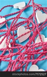 Creative closeup layout from red tangled rope and small white painted wooden hearts on a light blue background. Valentine&rsquo;s day greeting card.. Close-up background from red rope and white hearts.