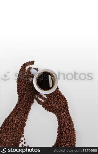 Creative coffee bean art; human hands made of roasted coffee beans, holding a coffee cup on grey background.