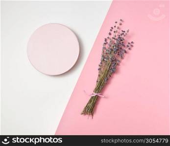 Creative composition from round board and natural lavender flowers branch on a duotone light grey pink background with copy space.. Decorative card with lavender bunch and round frame.