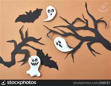 Creative composition of paper with flying bats and ghosts over tree branches on a brown background with space for text. Handcraft layout for Halloween. Flat lay. Paper tree branches flying ghosts and bats on a brown background with space for text. Scary handcraft layout to Halloween. Flat lay