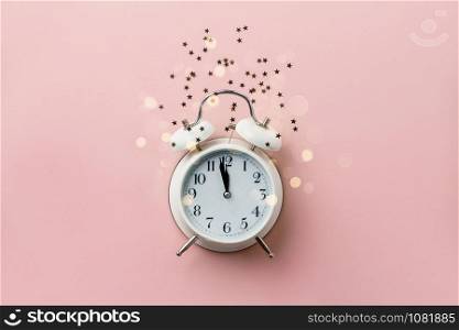 Creative composition with alarm clock and golden stars confetti on pink background. New Year Christmas Top view flat lay
