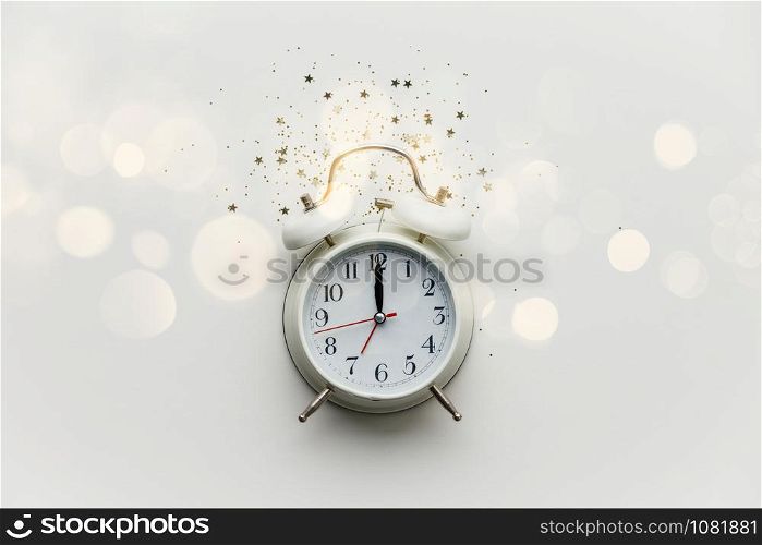 Creative composition with alarm clock and golden stars confetti on white background. New Year Christmas Top view flat lay