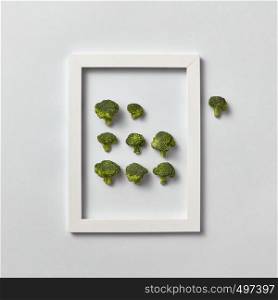 Creative composition with freshly picked green broccoli in a frame and one part out of it on a light gray background, place for text. Flat lay. Vegan concept.. Organic frame with fresh natural broccoli on a light gray background.