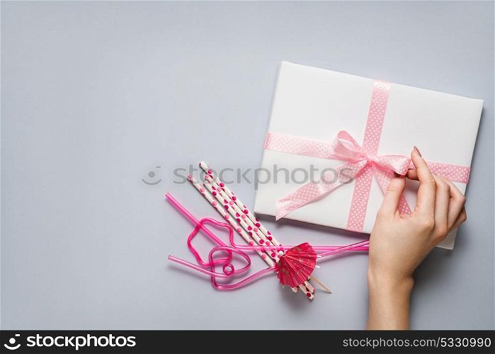 Creative concept photo of a present box with bow and cocktail straws on grey background.