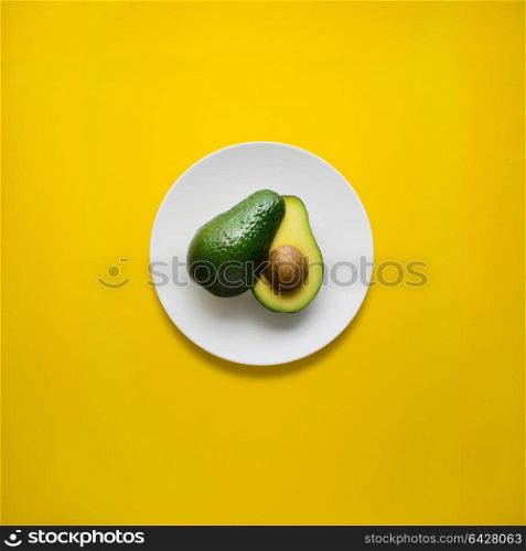 Creative concept photo of avocado on painted plate on yellow background.
