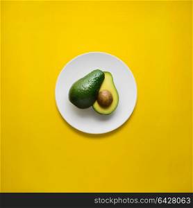 Creative concept photo of avocado on painted plate on yellow background.