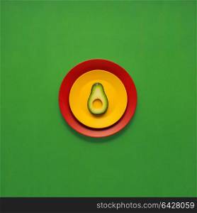 Creative concept photo of avocado slice on painted plates on green background.