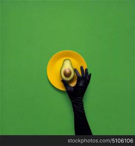 Creative concept photo of avocado with hand on painted plate on green background.