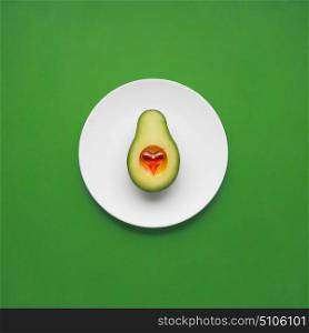 Creative concept photo of avocado with heart on painted plate on green background.