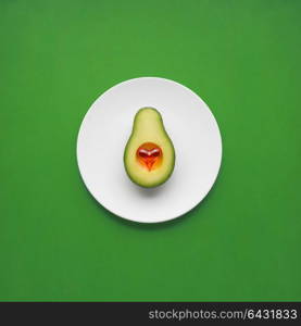 Creative concept photo of avocado with heart on painted plate on green background.