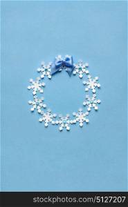 Creative concept photo of christmas wreath made of paper snowflakes on blue background.