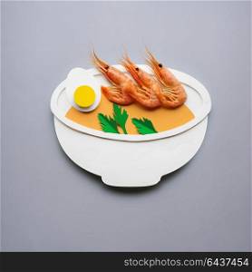 Creative concept photo of soup with shrimps made of paper on grey background.