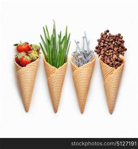 Creative concept photo of waffle cones filled with berries, onion, nails and coffee on white background.