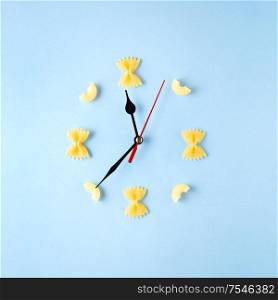 Creative concept still life food diet health photo of raw pasta spaghetti in shape of clock with hands on blue background.