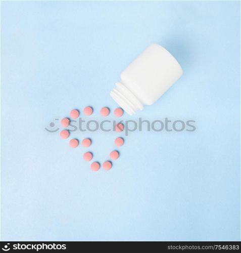 Creative concept still life health medicine photo of pills drugs cure in shape of heart with bottle on blue background.