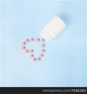 Creative concept still life health medicine photo of pills drugs cure in shape of heart with bottle on blue background.