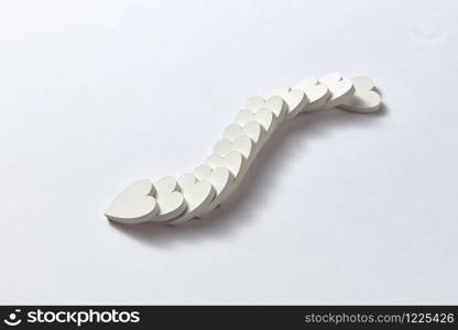Creative curve chain from gypsum hearts in the shape of snake on a light gray background with soft shadows, copy space. Valentine&rsquo;s greeting card.. Curve chain from plaster hearts in the shape of snake.