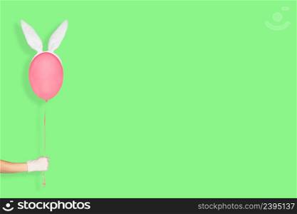 Creative easter minimal concept. Hand in white glove holding a pink balloon in bunny ears isolated on pastel green background. Easter Banner with copy space.. Creative easter minimal concept. Hand in white glove holding a pink balloon in bunny ears isolated on pastel green background. Easter Banner with copy space
