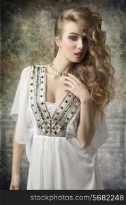 creative fashion portrait of beauty woman with antique dress and golden jewellery posing with curly long hair and stylish make-up