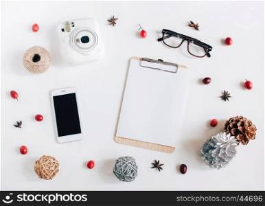 Creative flat lay of blank clipboard, smartphone, instant camera with autumn ornaments on white background, top view