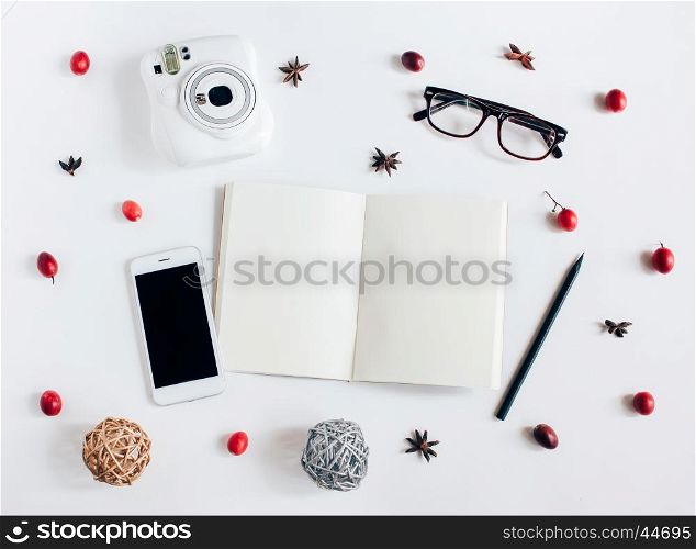 Creative flat lay of blank notebook, smartphone, instant camera with autumn ornaments on white background, top view
