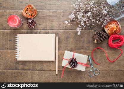 Creative flat lay of Christmas gift box, ornaments, winter accessories and craft notebook on wood background, Top view