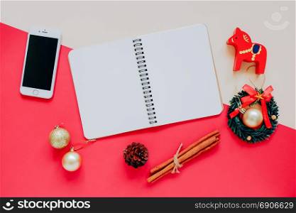 Creative flat lay of craft and blank notebook mock up with christmas ornaments and smartphone on colorful background, minimal style