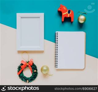 Creative flat lay of craft and photo frame, blank notebook mock up with christmas ornaments and gift box on colorful background, minimal style