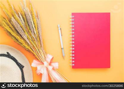 Creative flat lay of red color diary book, pen, dried flowers and woman hat on orange color background, Lifestyle, Summer concept