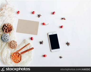 Creative flat lay of smartphone and greeting card with autumn ornaments on white background, top view