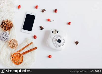 Creative flat lay of smartphone and instant camera with autumn ornaments on white background, top view
