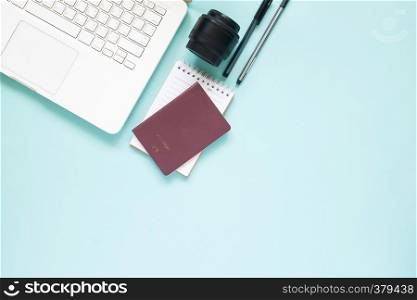 Creative flat lay of workspace desk with laptop, passport and camera lens on blue colour background. Travel lifestyle concept