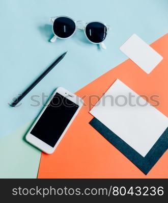 Creative flat lay of workspace desk with smartphone, envelope, name card and sunglasses on minimal color background
