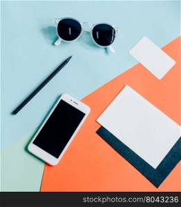Creative flat lay of workspace desk with smartphone, envelope, name card and sunglasses on minimal color background