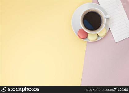 Creative flat lay photo of coffee cup and macaroons and empty list with copy space on pink background minimal style