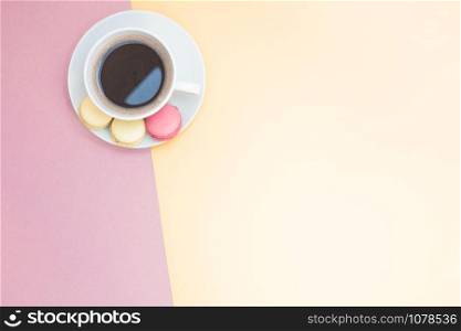 Creative flat lay photo of coffee cup and macaroons with copy space on pink and yellow background minimal style