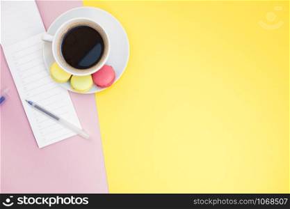 Creative flat lay photo of coffee cup with macaroons and a notepad with copy space on pink and yellow background minimal style