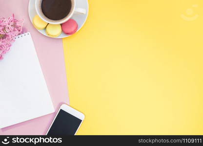 Creative flat lay photo of coffee cup with macaroons and a notepad with copy space on pink and yellow background minimal style