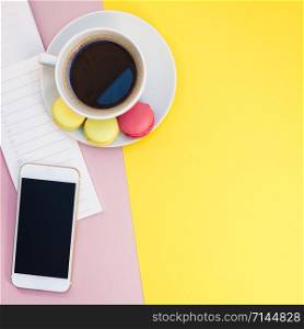 Creative flat lay photo of coffee cup with macaroons and a notepad with copy space on pink and yellow background minimal style