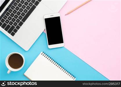 Creative flat lay photo of workspace desk. Top view office desk with laptop, phone, pencil, notebook and coffee cup on blue pink color background. Top view with copy space, flat lay photography.