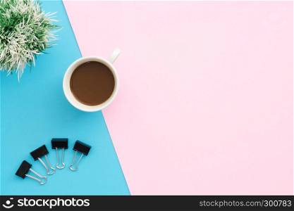 Creative flat lay photo of workspace desk. Top view office desk with clip, plant and coffee cup on blue pink color background. Top view with copy space, flat lay photography.