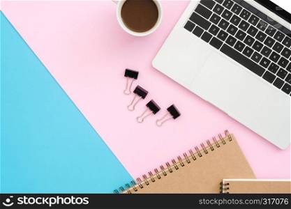 Creative flat lay photo of workspace desk. Top view office desk with laptop, clip, notebook and coffee cup on blue pink color background. Top view with copy space, flat lay photography.