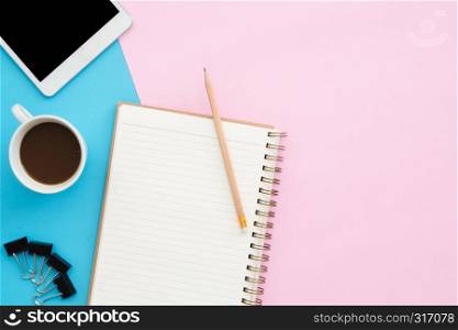Creative flat lay photo of workspace desk. Top view office desk with tablet, pencil, notebook and coffee cup on blue pink color background. Top view with copy space, flat lay photography.