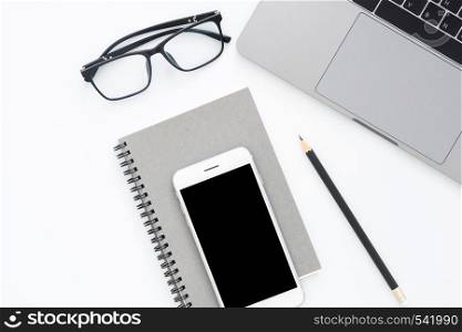 Creative flat lay photo of workspace desk. Top view office desk with laptop, blank phone, pencil, notebook and glasses on white color background. Top view with copy space, flat lay photography.