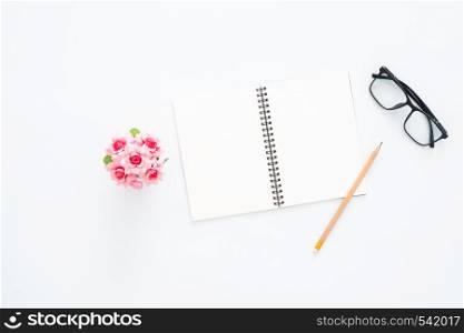 Creative flat lay photo of workspace desk. Top view office desk with glasses, pencil, blank notebook and plant on white color background. Top view with copy space, flat lay photography.