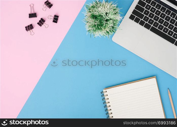 Creative flat lay photo of workspace desk. Top view office desk with laptop, pencil, notebook and plant on blue pink color background. Top view with copy space, flat lay photography.