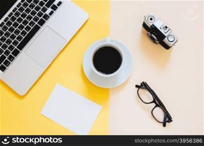 Creative flat lay photo of workspace desk with laptop, blank paper, coffee, eyeglasses and film camera on yellow modern background&#xD;