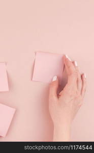 Creative flat lay photo of workspace desk with millennial pink sticker paper post it mock up in woman hands holding and gluing them on wall with copy space background minimal style. Template for text